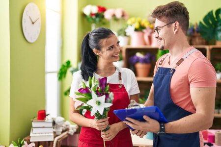 Photo for Man and woman florists holding bouquet of flowers and clipboard at flower shop - Royalty Free Image