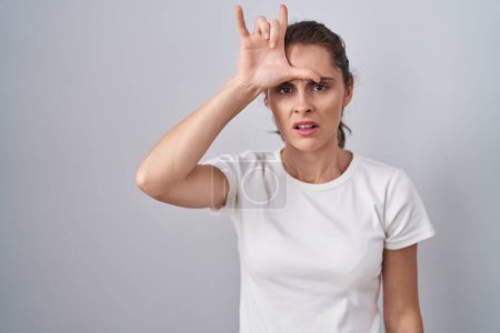 Téléchargez les photos : Beautiful brunette woman standing over isolated background making fun of people with fingers on forehead doing loser gesture mocking and insulting. - en image libre de droit