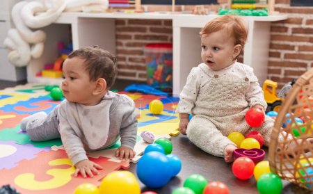 Foto de Dos adorables bebés jugando con bolas sentados en el suelo en el jardín de infantes - Imagen libre de derechos