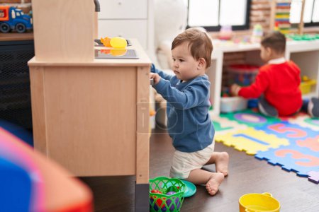 Photo for Adorable caucasian baby playing with play kitchen sitting on floor at kindergarten - Royalty Free Image