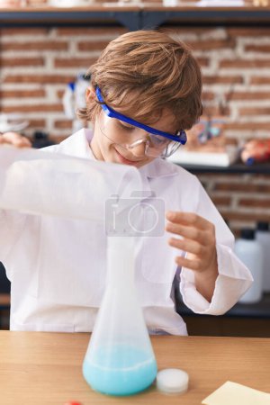 Foto de Adorable caucásico chico estudiante verter líquido en tubo de ensayo en el aula - Imagen libre de derechos