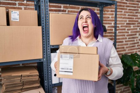 Téléchargez les photos : Plus size woman wit purple hair working at small business ecommerce holding boxes angry and mad screaming frustrated and furious, shouting with anger looking up. - en image libre de droit