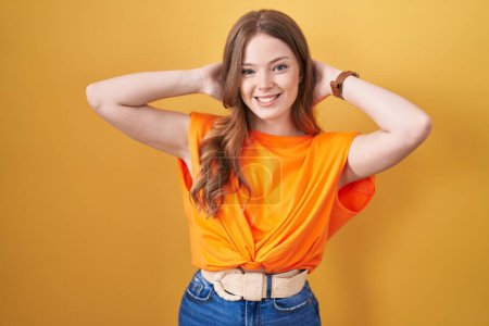 Photo for Caucasian woman standing over yellow background relaxing and stretching, arms and hands behind head and neck smiling happy - Royalty Free Image