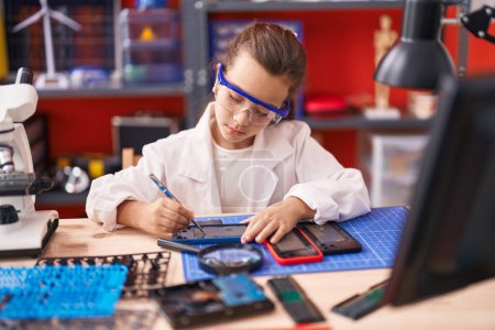 Photo for Adorable hispanic girl student repairing smartphone at classroom - Royalty Free Image