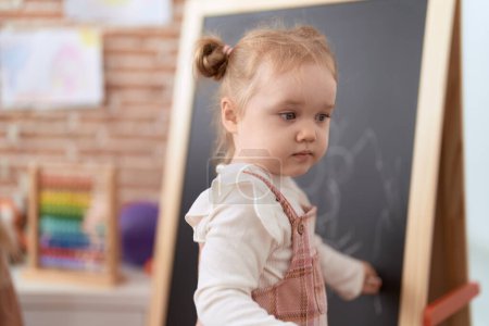 Photo for Adorable caucasian girl drawing on blackboard standing at kindergarten - Royalty Free Image