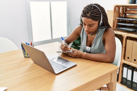 Photo for Young african american woman call center agent writing on notebook at office - Royalty Free Image