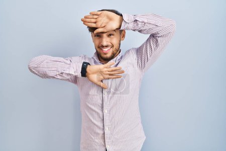 Photo pour Arab man with beard standing over blue background smiling cheerful playing peek a boo with hands showing face. surprised and exited - image libre de droit
