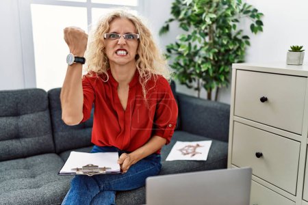 Photo for Middle age psychologist woman at consultation office angry and mad raising fist frustrated and furious while shouting with anger. rage and aggressive concept. - Royalty Free Image