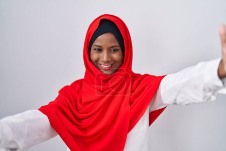 Photo for Young arab woman wearing traditional islamic hijab scarf looking at the camera smiling with open arms for hug. cheerful expression embracing happiness. - Royalty Free Image