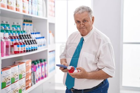 Téléchargez les photos : Moyen âge homme aux cheveux gris client utilisant smartphone tenant bouteille de médicament à la pharmacie - en image libre de droit