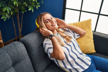 Photo for Young blonde woman listening to music relaxed on sofa at home - Royalty Free Image