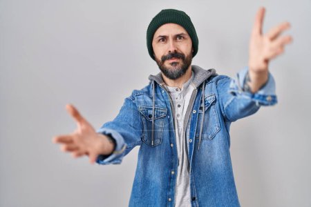 Téléchargez les photos : Young hispanic man with tattoos wearing wool cap looking at the camera smiling with open arms for hug. cheerful expression embracing happiness. - en image libre de droit