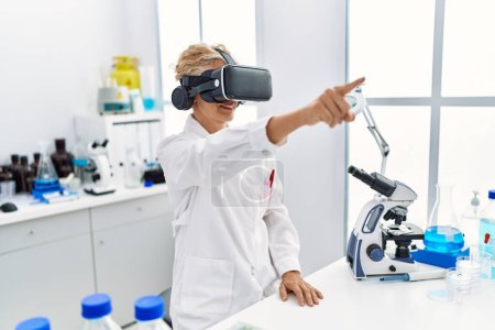 Téléchargez les photos : Femme blonde d'âge moyen portant l'uniforme de scientifique en utilisant des lunettes vr travaillant au laboratoire - en image libre de droit