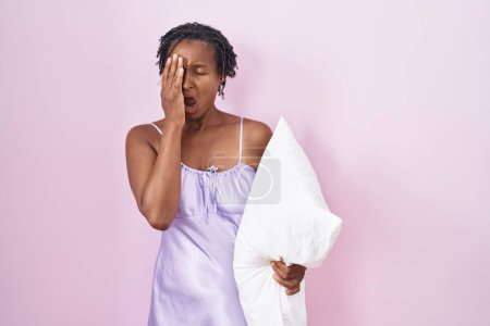 Photo for African woman with dreadlocks wearing pajama hugging pillow yawning tired covering half face, eye and mouth with hand. face hurts in pain. - Royalty Free Image