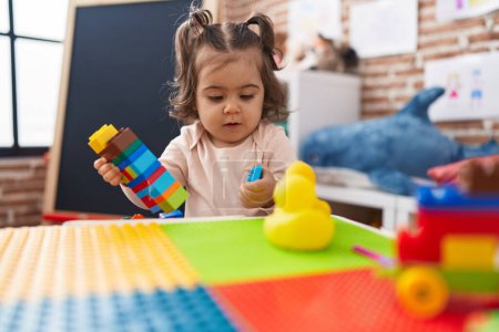 Téléchargez les photos : Adorable fille hispanique jouer avec des blocs de construction debout à la maternelle - en image libre de droit