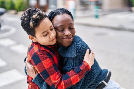 Téléchargez les photos : Afro-américaine mère et fils souriant confiant étreignant l'autre à la rue - en image libre de droit