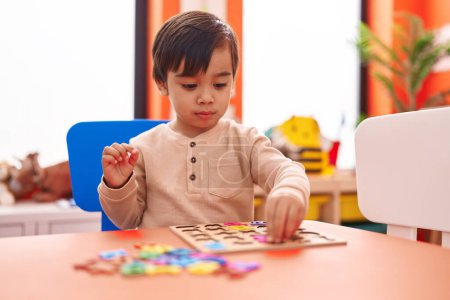 Téléchargez les photos : Adorable garçon hispanique jouer avec des mathématiques jeu de puzzle assis sur la table à la maternelle - en image libre de droit