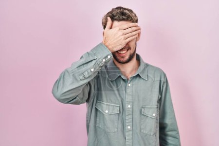 Photo for Hispanic man with beard standing over pink background smiling and laughing with hand on face covering eyes for surprise. blind concept. - Royalty Free Image