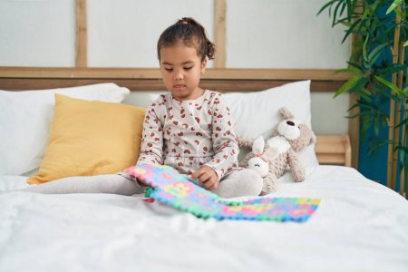 Foto de Adorable chica hispana jugando matemáticas juego sentado en la cama en el dormitorio - Imagen libre de derechos