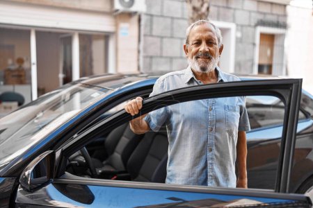 Foto de Hombre de pelo gris mayor sonriendo confiado abriendo la puerta del coche en la calle - Imagen libre de derechos