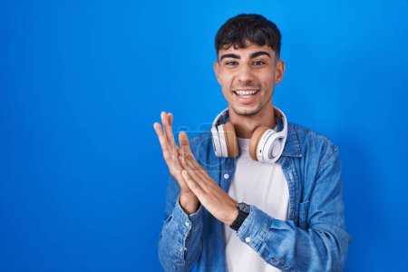 Téléchargez les photos : Young hispanic man standing over blue background clapping and applauding happy and joyful, smiling proud hands together - en image libre de droit