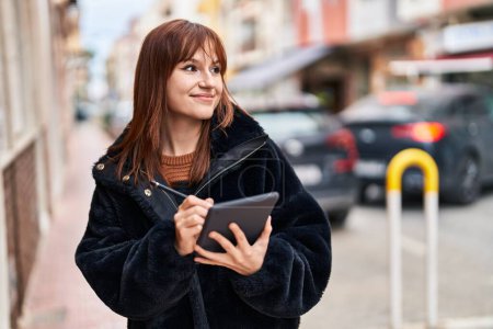 Foto de Mujer joven sonriendo confiada usando touchpad en la calle - Imagen libre de derechos