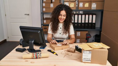 Photo for Young beautiful hispanic woman ecommerce business worker smiling confident prepare package at office - Royalty Free Image