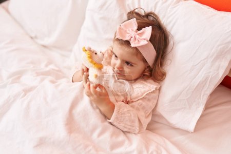 Foto de Adorable rubio niño jugando con juguetes acostado en la cama en el dormitorio - Imagen libre de derechos
