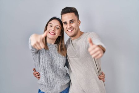 Photo for Young hispanic couple standing over white background approving doing positive gesture with hand, thumbs up smiling and happy for success. winner gesture. - Royalty Free Image