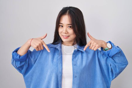 Foto de Young chinese woman standing over white background looking confident with smile on face, pointing oneself with fingers proud and happy. - Imagen libre de derechos