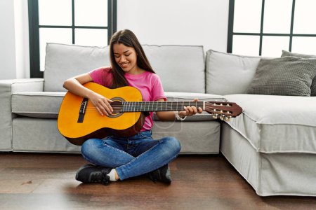 Photo for Young latin woman playing classical guitar sitting on floor at home - Royalty Free Image