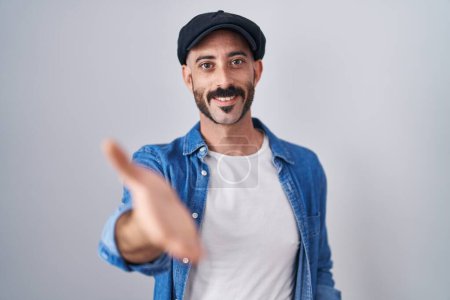 Foto de Hombre hispano con barba de pie sobre fondo aislado sonriente alegre ofreciendo mano de palma dando asistencia y aceptación. - Imagen libre de derechos