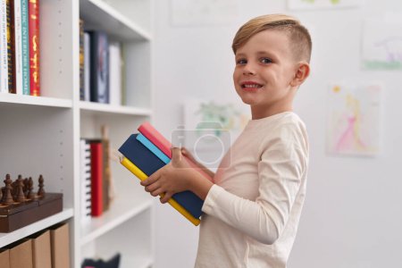 Photo for Adorable toddler smiling confident holding books at classroom - Royalty Free Image