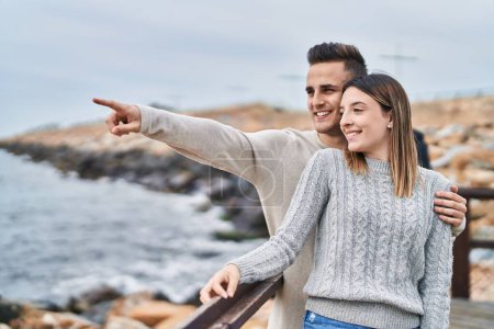 Téléchargez les photos : Homme et femme couple étreignant l'un l'autre pointant du doigt au bord de la mer - en image libre de droit
