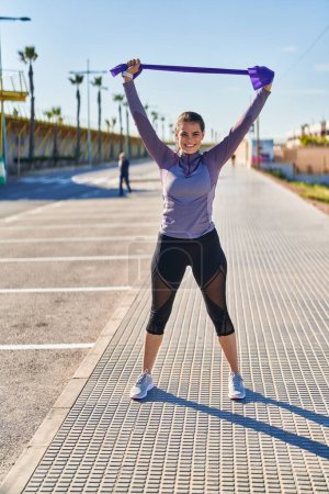 Photo for Young beautiful hispanic woman stretching arms using elastic band at street - Royalty Free Image