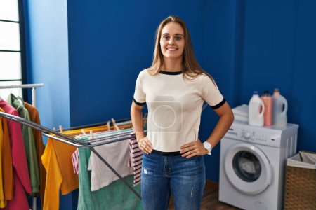 Foto de Joven mujer rubia sonriendo confiada de pie en la lavandería - Imagen libre de derechos