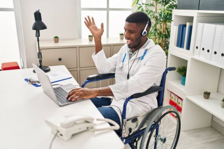 Photo for African american doctor man working on online appointment sitting on wheelchair celebrating achievement with happy smile and winner expression with raised hand - Royalty Free Image
