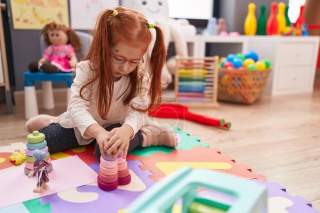 Téléchargez les photos : Adorable rousse fille jouer avec des jouets assis sur le sol à la maternelle - en image libre de droit