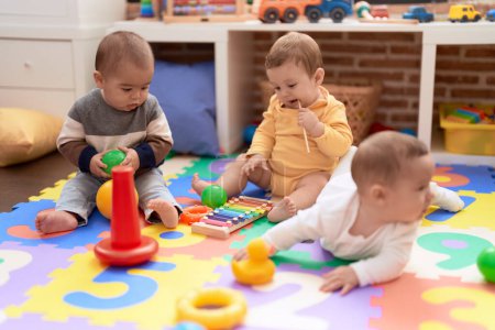 Téléchargez les photos : Groupe de tout-petits jouant avec des jouets assis sur le sol à la maternelle - en image libre de droit