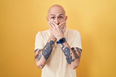 Téléchargez les photos : Hispanic man with tattoos standing over yellow background shocked covering mouth with hands for mistake. secret concept. - en image libre de droit