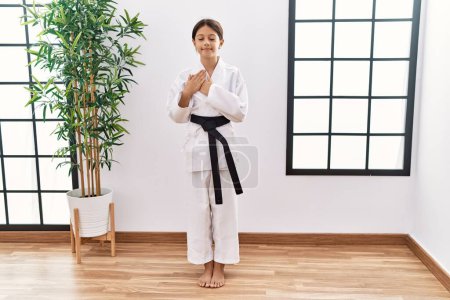 Téléchargez les photos : Young hispanic girl wearing karate kimono and black belt smiling with hands on chest with closed eyes and grateful gesture on face. health concept. - en image libre de droit