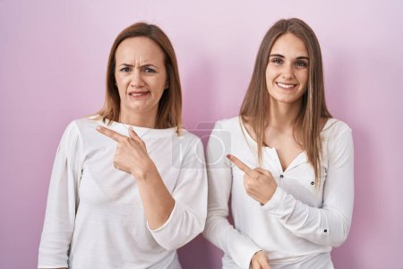 Téléchargez les photos : Middle age mother and young daughter standing over pink background pointing aside worried and nervous with forefinger, concerned and surprised expression - en image libre de droit