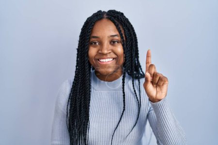 Téléchargez les photos : African american woman standing over blue background showing and pointing up with finger number one while smiling confident and happy. - en image libre de droit