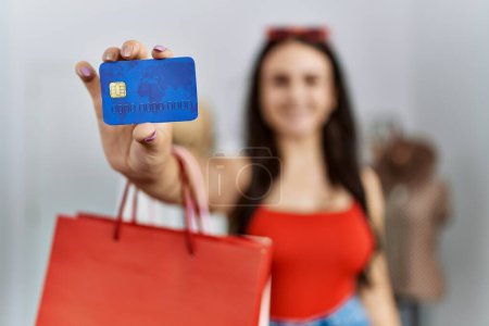 Foto de Joven mujer caucásica sosteniendo compras con tarjeta de crédito en tienda de ropa - Imagen libre de derechos