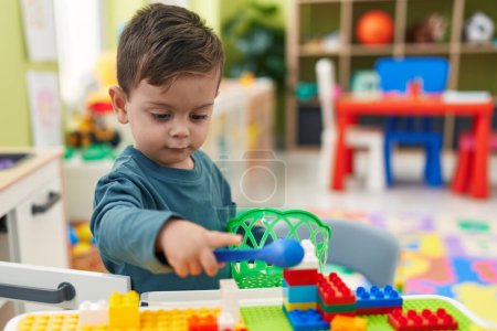 Photo for Adorable hispanic boy playing with play kitchen standing at kindergarten - Royalty Free Image