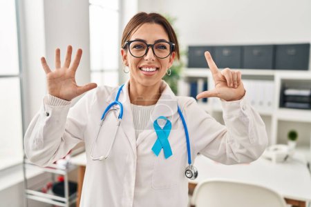 Téléchargez les photos : Jeune femme brune médecin portant stéthoscope à la clinique montrant et pointant vers le haut avec les doigts numéro sept tout en souriant confiant et heureux. - en image libre de droit