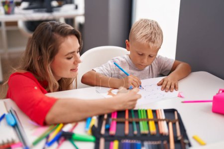 Foto de Profesor y niño pequeño sentados en la mesa dibujando sobre papel en el aula - Imagen libre de derechos