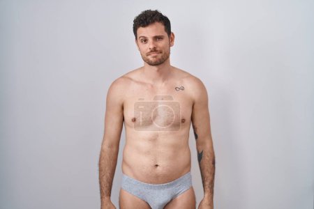 Téléchargez les photos : Young hispanic man standing shirtless wearing underware looking sleepy and tired, exhausted for fatigue and hangover, lazy eyes in the morning. - en image libre de droit