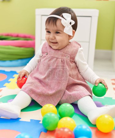 Photo for Adorable hispanic baby playing with balls sitting on floor at kindergarten - Royalty Free Image