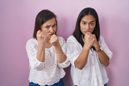 Foto de Madre e hija hispanas juntas listas para luchar con el gesto de defensa del puño, cara enojada y molesta, temerosas del problema - Imagen libre de derechos